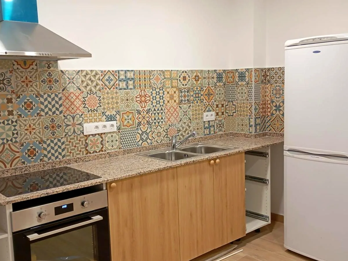 Renovated kitchen with multicolour hydraulic tile splashback, granite worktop and wooden units — Grupo Topo Reformas